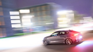 Ein sportliches Auto fährt vor verwischtem Hintergrund auf einer Straße.