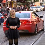 Eine Frau mit dunklen Haaren vor einem roten Auto auf einer Straße.