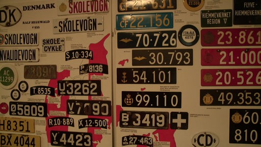 Mehrere Nummernschilder ausgestellt an einer Wand.
