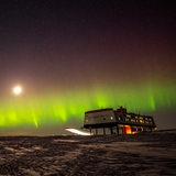 Polarlichter leuchten hinter einer Forschungsstation in der Antarktis.