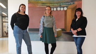 Joanna Hezel, Nele Oetzmann und Natasha Köhn stehen vor einem Gemälde.