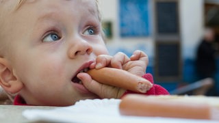 Ein Baby isst eine Wurst.