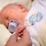 Ein neugeborenes Baby mit einem Schnuller im Mund hält eine Hand