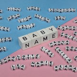 Vier Würfel in der Mitte des Bildes zeigen das Wort "BABY NAME", rundherum liegen viele weitere kleinere Würfel, die andere Namen zeigen.