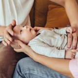 Ein Baby liegt auf den Knien der Mutter, während eine zweite Frau dem Baby den Bauch massiert.