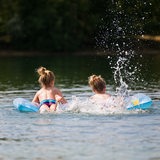Kinder baden mit Luftmatratze in einem See.