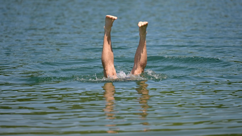Ein Mensch springt in einem Badesee. Aus dem See ragen nur die Beine.