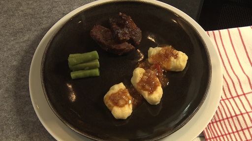Bäckchen vom Angus-Rind zusammen mit Kartoffelpüree und grünen Bohnen auf einem schwarzen Teller.
