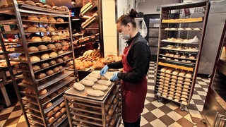 Eine Bäckereifachverkäuferin steht in einer Bäckerei und wendet Teigrohlinge auf einem Blech.