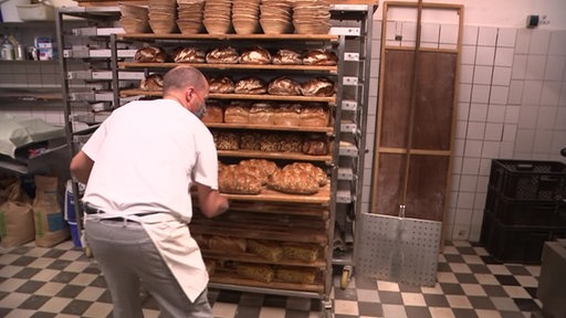 Ein Bäcker legt ein Tablett mit frisch gebackenem Brot in das Brotregal.