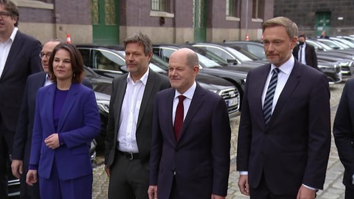 Baerbock, Habeck, Scholz und Lindner auf einem Parkplatz. Sie tragen Anzüge.