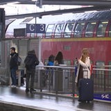 Personen warten am Gleis auf ihre Bahn.