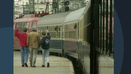 Eine Archivaufnahme eines Bahnsteiges, auf dem einige Personen einem ausfahrenden Zug hinterherwinken.