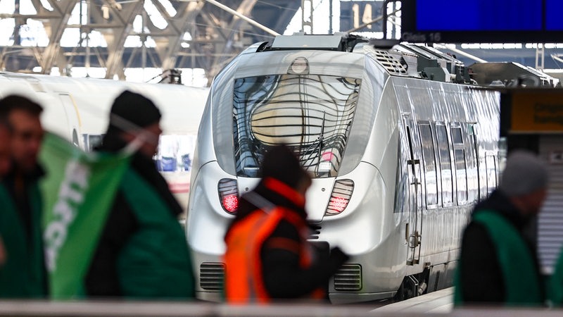 Streikende Lokführer gehen durch den Leipziger Hauptbahnhof vor einem ICE entlang.
