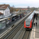 Ein Regionalzug fährt in einen Bahnhof ein. Wenig Menschen stehen an den Bahngleisen.