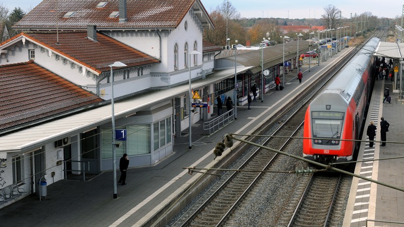 Ein Regionalzug fährt in einen Bahnhof ein. Wenig Menschen stehen an den Bahngleisen.