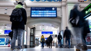 Reisende schauen am Bremer Hauptbahnhof auf die Informationstafel zu den Abfahrten. 