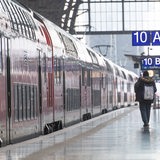 Ein Mann schlendert an einem wartenden Zug ein Bahngleis entlang.