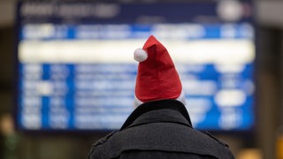 Ein Mann mit Weihnachtsmannmütze geht am Hauptbahnhof auf die Anzeigetafel zu.