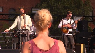 Eine Frau steht mit dem Rücken zur Kamera, vor ihr eine Band.