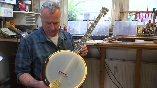 Der Berühmte Banjobauer Norbert Pietsch hält ein Banjo in seiner Hand. 