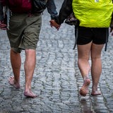 Ein Paar geht barfuß bei Regenwetter über Kopfsteinpflaster.