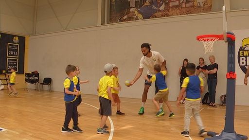Kinder spielen mit einem Erwachsenen in einer Halle Basketball.