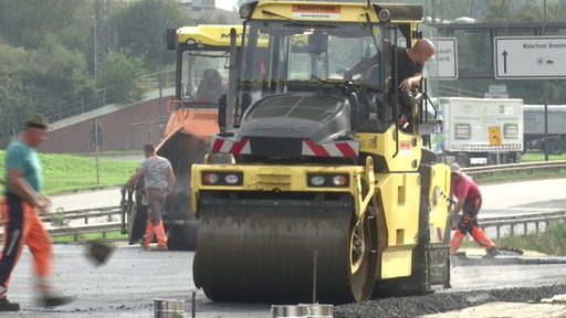 Es sind Bauarbeiten einer neuen Straße zu sehen. Eine Walze verdichtet den Asphalt.