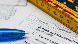 Auf einem Antrag auf Baugenehmigung liegt ein Maßstab und ein Kugelschreiber.
