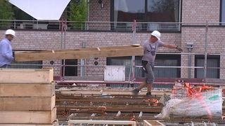 Zwei Bauarbeiter tragen auf einer Hausbaustelle Holz.