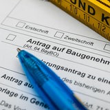 Ein blauer Kugelschreiber liegt auf einem Antrag für eine Baugenehmigung, daneben ein Maßstab.