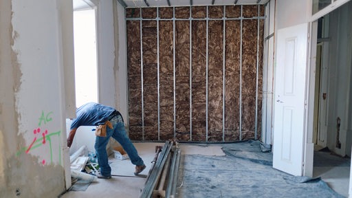 Bauarbeiter arbeitet auf einer Innen-Baustelle, Dämmung an einer Wand im Hintergrund