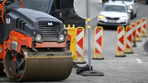 Straßenbaustelle mit Absperrungen und einer Asphaltierungsraupe im Vordergrund