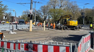 In einem abgesperrten Kreuzungsbereichs sind große Baugeräte und mehrere Bauarbeiter im Einsatz