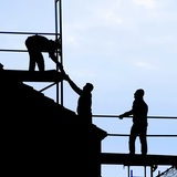 Dachdecker führen Arbeiten an einem Reihenhaus in Bremen durch. Sie sind nur als Silhouette vor dem hellen Himmel zu sehen.