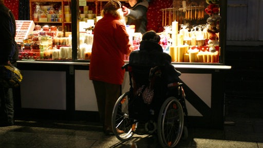 Eine Frau im Rollstuhl an einem Kerzenstand auf dem Weihnachtsmarkt.