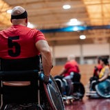 Personen in Rollstühlen spielen einen Ballsport in einer Sportalle (Symbolbild)
