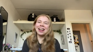 Die Bremer Para-Sportlerin Mascha Mosel sitzt mit strahlendem Lachen in ihrem Schlafzimmer und nimmt eine Videobotschaft auf, um für die Spenden zu danken.