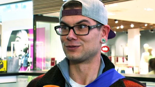 Ein junger Mann mit Cap vor einem Bekleidungsgeschäft im Interview mit buten un binnen