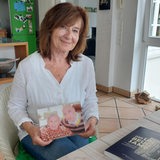 Eine Frau sitzt an einem Tisch und hält ein Foto in den Händen.
