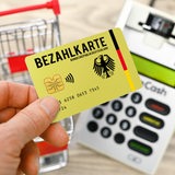 eine Hand mit Bezahlkarte vor einem Kartenlesegerät