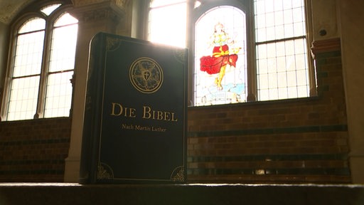 Die Bibel vor einem bunten Kirchenfenster.