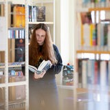 Junge Frau liest in ein Buch in einer Bibliothek (Symbolbild)