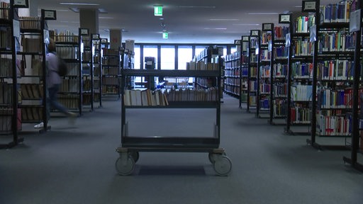 Rechts und links sind viele Regale mit Büchern, in der Mitte steht ein Wagen mit Büchern in der Bremer Universitätsbibliothek. 