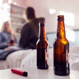 Zwei offene Bierflaschen stehen auf einem Tisch, im Hintergrund unterhalten sich zwei junge Frauen
