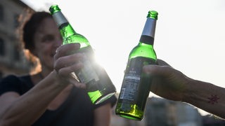 Zwei Menschen stoßen mit Bierflaschen in der Abendsonne an.
