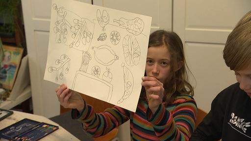 Ein Mädchen hält ein Bild mit gemalten Früchten hoch