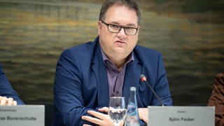 Bremens Finanzsenator Björn Fecker (Grüne) sitzt hinter einem Mikrofon