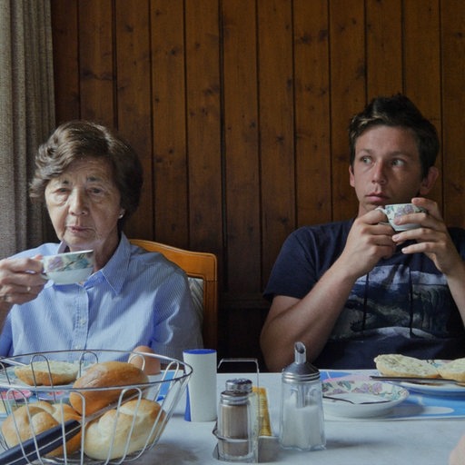 Eine alte Fraue sitzt am Frühstückstisch neben ihr ein junger Mann
