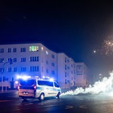 Ein Polizeifahrzeug fährt an rauchenden Böllnern vorbei.